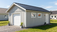 Attefallsgarage med vit garageport, sidodörr och fönster, svart takplåt