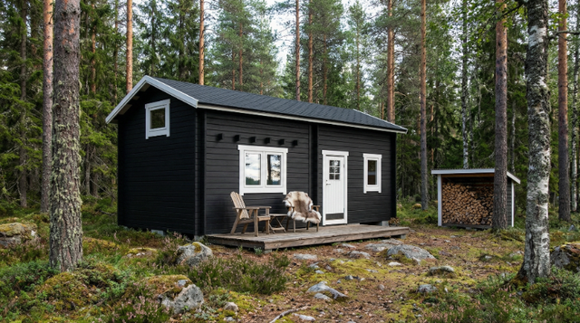 Attefallshus med mörk fasad, vita fönster och entrédörr samt trallad uteplats.