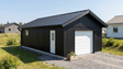 Enkelgarage i mörkgrå panel med vit garageport och sidodörr samt fönster